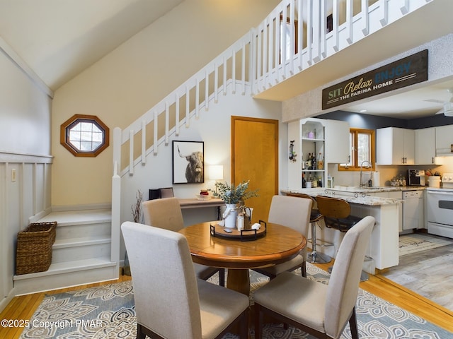 dining room featuring sink, light hardwood / wood-style flooring, high vaulted ceiling, and a healthy amount of sunlight