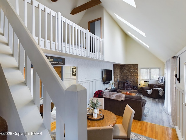 dining space with hardwood / wood-style flooring, a fireplace, a skylight, and high vaulted ceiling