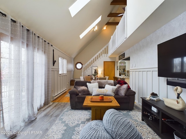 living room featuring a baseboard heating unit, hardwood / wood-style floors, high vaulted ceiling, and a skylight