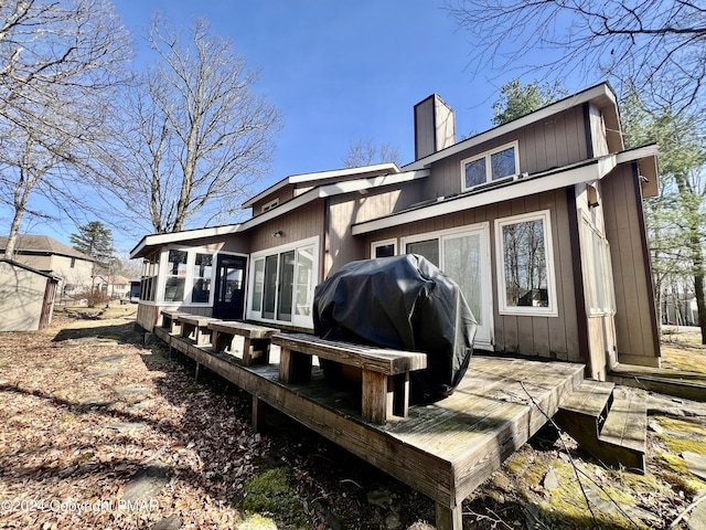 rear view of property featuring a wooden deck, a chimney, and a sunroom