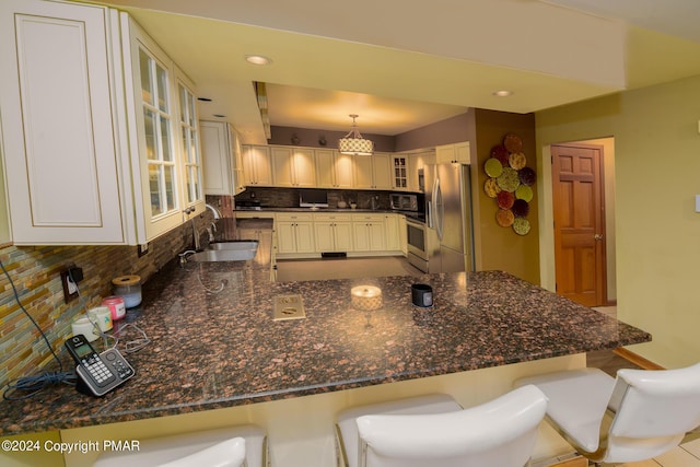 kitchen featuring decorative backsplash, a sink, stainless steel appliances, a peninsula, and glass insert cabinets