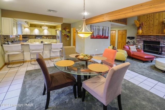 dining space featuring a brick fireplace, light tile patterned floors, beamed ceiling, and visible vents