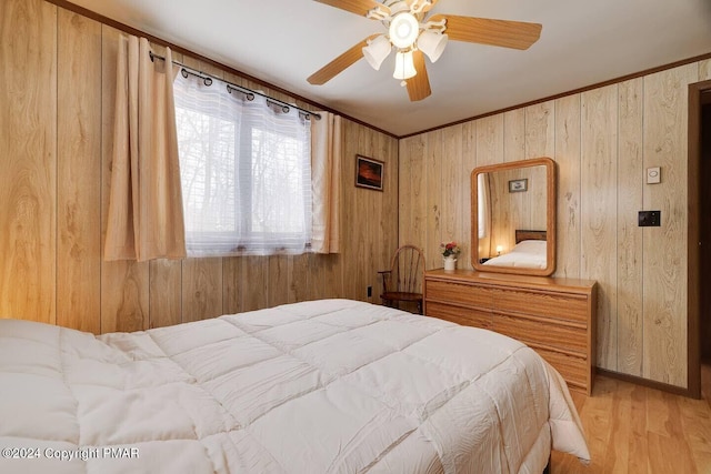 bedroom with a ceiling fan, wood walls, light wood finished floors, and ornamental molding