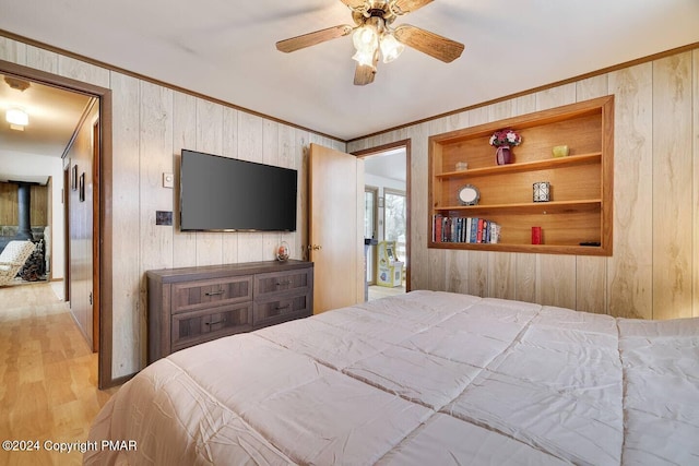 bedroom featuring ceiling fan, light wood-style flooring, wood walls, and ornamental molding