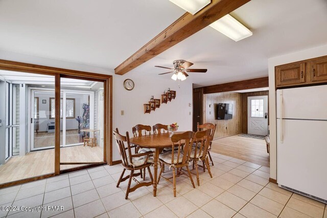 dining room featuring beamed ceiling, light tile patterned floors, wood walls, and ceiling fan