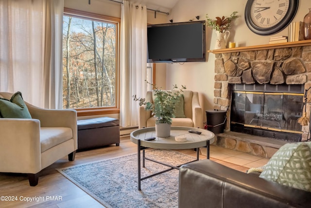 living area with a baseboard radiator, vaulted ceiling, wood finished floors, and a stone fireplace