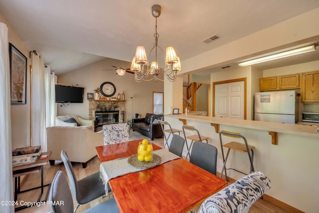 dining space featuring a fireplace, lofted ceiling, visible vents, wood finished floors, and ceiling fan with notable chandelier