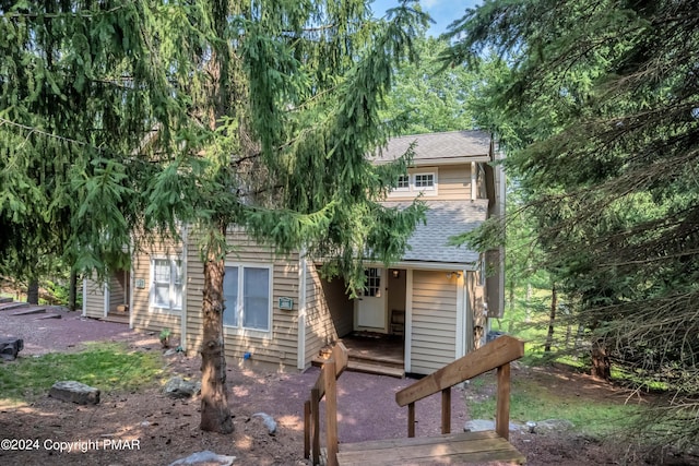 view of property hidden behind natural elements with a shingled roof