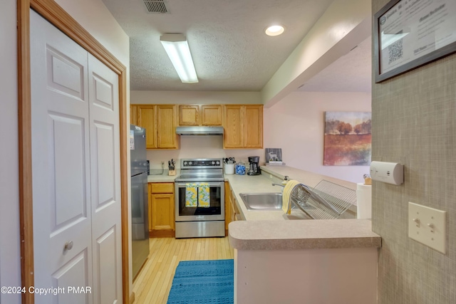 kitchen with refrigerator, light countertops, a sink, stainless steel range with electric stovetop, and under cabinet range hood