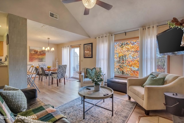 living area with lofted ceiling, a baseboard radiator, visible vents, wood finished floors, and ceiling fan with notable chandelier