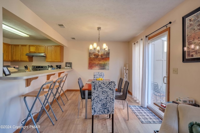 dining area with light wood finished floors, baseboards, visible vents, an inviting chandelier, and a textured ceiling