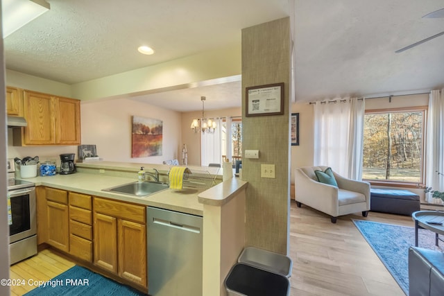 kitchen featuring a notable chandelier, stainless steel appliances, a sink, a peninsula, and under cabinet range hood