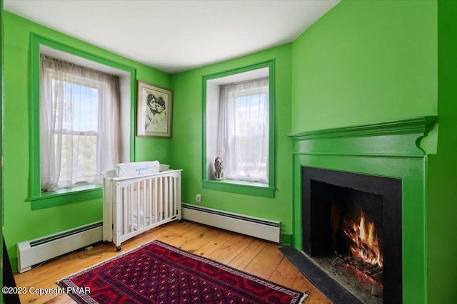 bedroom featuring hardwood / wood-style floors, baseboard heating, and a fireplace with flush hearth