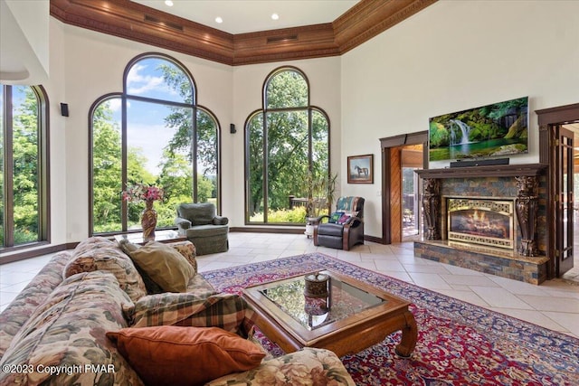 living area with baseboards, a glass covered fireplace, a towering ceiling, tile patterned floors, and crown molding