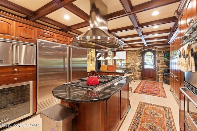 kitchen featuring a center island, stainless steel appliances, island range hood, dark stone counters, and coffered ceiling