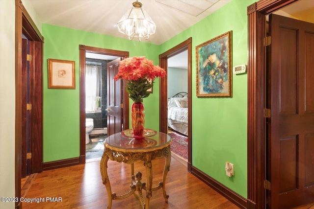 hall with an inviting chandelier, wood finished floors, and baseboards