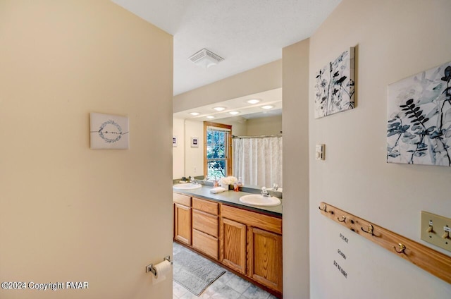 bathroom with double vanity, a shower with curtain, visible vents, and a sink