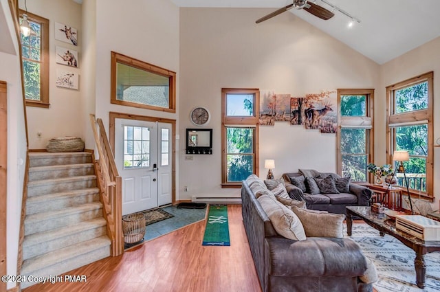 living room with a baseboard radiator, rail lighting, stairway, wood finished floors, and high vaulted ceiling