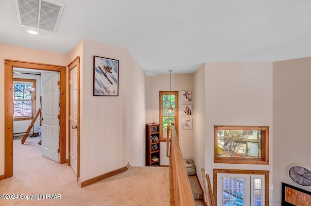 hallway featuring baseboards, visible vents, light carpet, and an upstairs landing