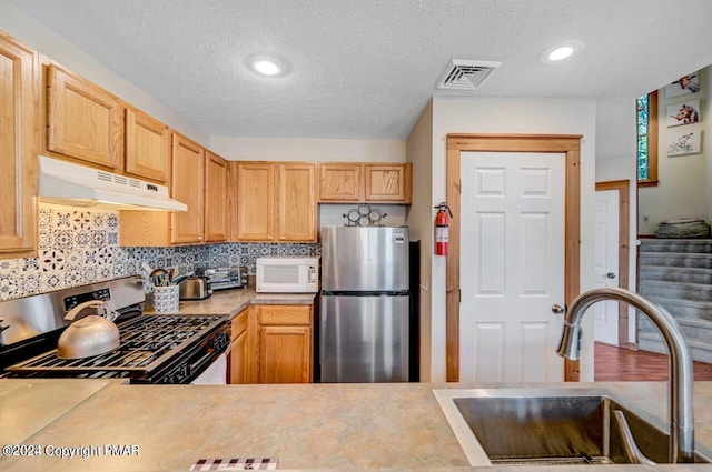 kitchen featuring decorative backsplash, appliances with stainless steel finishes, light countertops, under cabinet range hood, and a sink