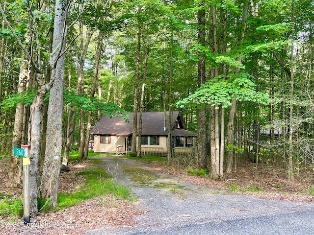 view of front of home with a shingled roof, driveway, and a view of trees