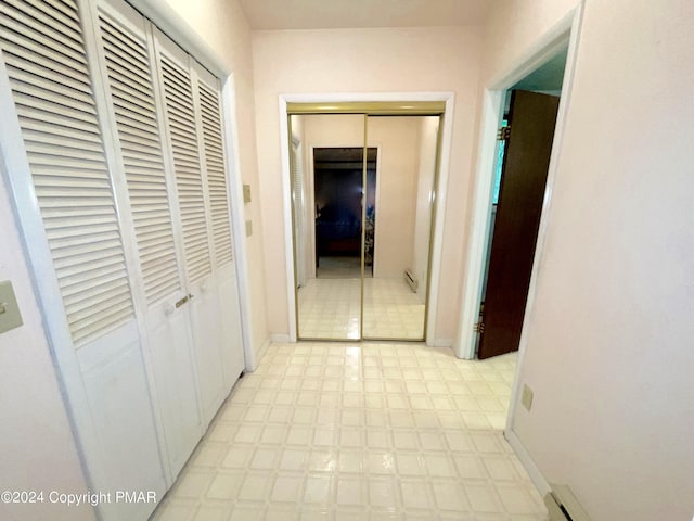 corridor featuring light floors, baseboard heating, and baseboards