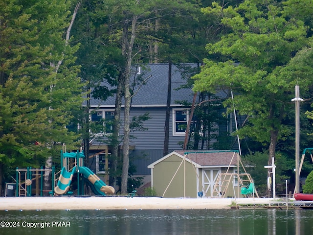 exterior space featuring a shingled roof, playground community, a water view, and an outdoor structure