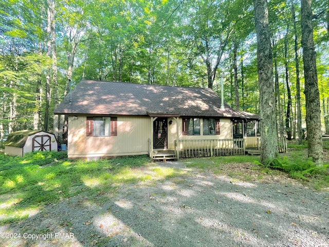 view of front of property featuring driveway, a shed, roof with shingles, and an outbuilding