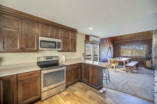 kitchen featuring a wall mounted air conditioner, a peninsula, stainless steel appliances, light countertops, and light wood-type flooring