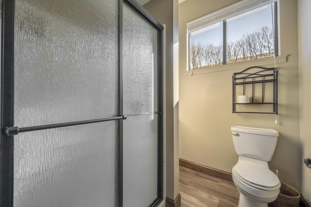 bathroom with toilet, a stall shower, baseboards, and wood finished floors