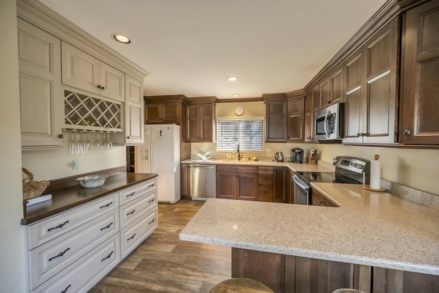 kitchen featuring light stone counters, appliances with stainless steel finishes, a sink, dark brown cabinets, and wood finished floors