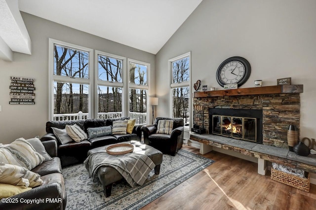 living room featuring hardwood / wood-style flooring, a stone fireplace, and high vaulted ceiling