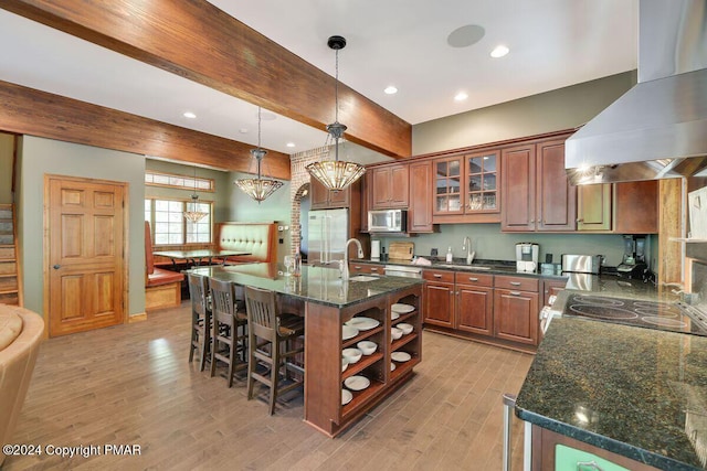 kitchen with a kitchen bar, stainless steel microwave, light wood finished floors, and wall chimney exhaust hood