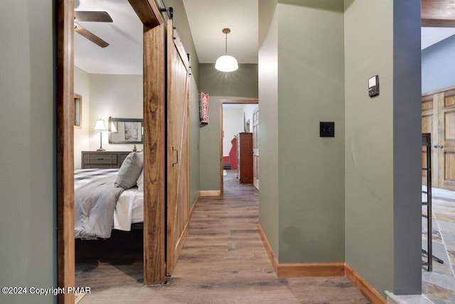 hallway featuring a barn door, baseboards, and wood finished floors