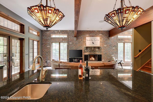 kitchen featuring a chandelier, brick wall, a sink, beamed ceiling, and dark stone countertops