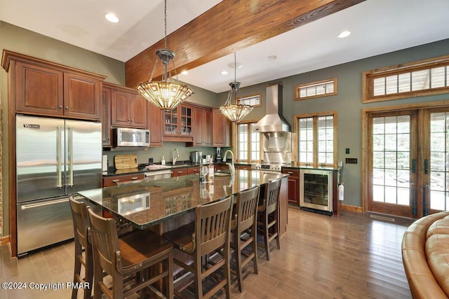 kitchen with wine cooler, a breakfast bar, appliances with stainless steel finishes, wall chimney range hood, and light wood-type flooring