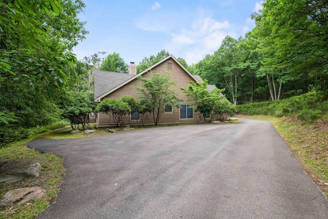 chalet / cabin featuring driveway, a shingled roof, and a chimney