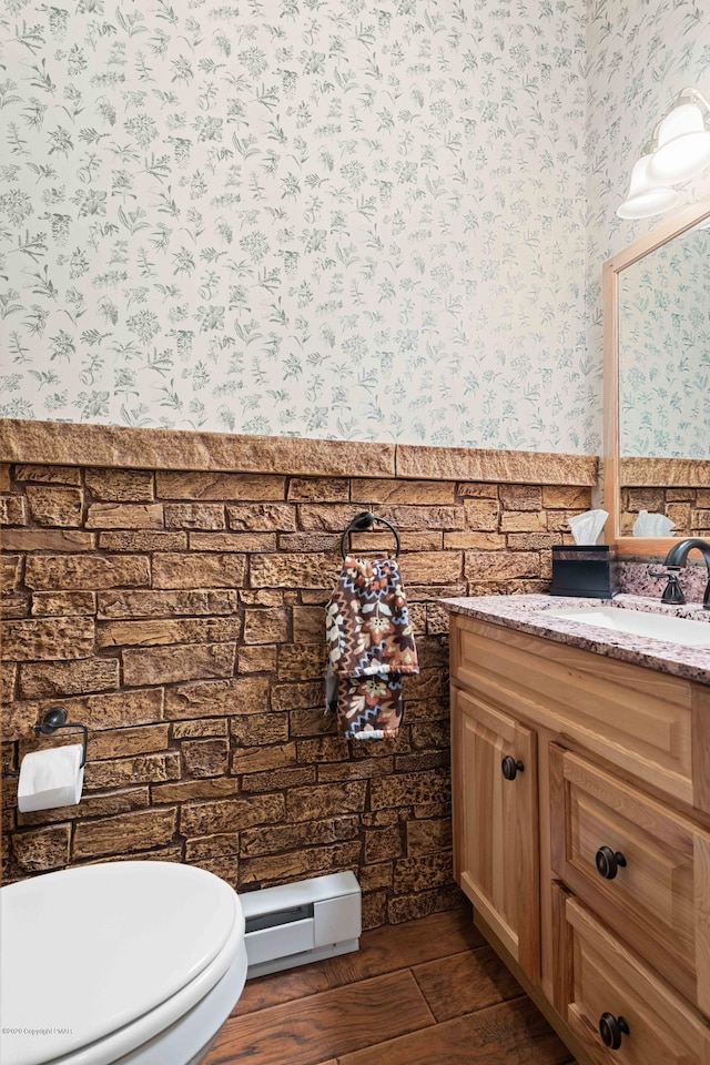 bathroom with wallpapered walls, a wainscoted wall, wood finished floors, vanity, and a baseboard heating unit