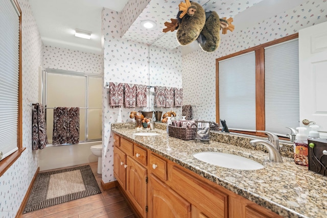 full bathroom featuring double vanity, a sink, toilet, and wallpapered walls