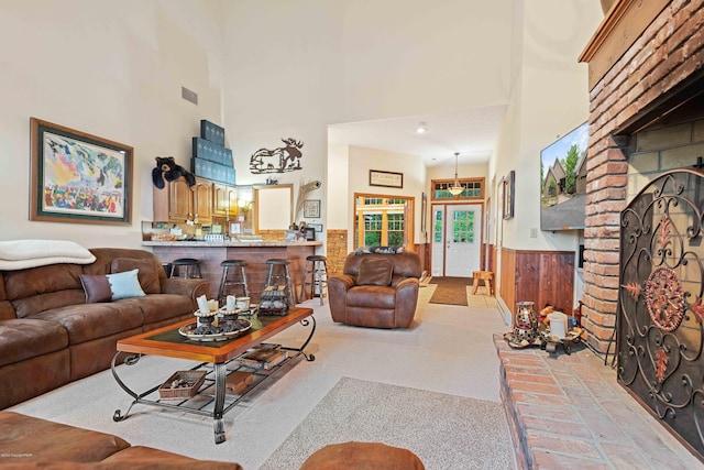 carpeted living room with wood walls, a towering ceiling, visible vents, wainscoting, and a brick fireplace