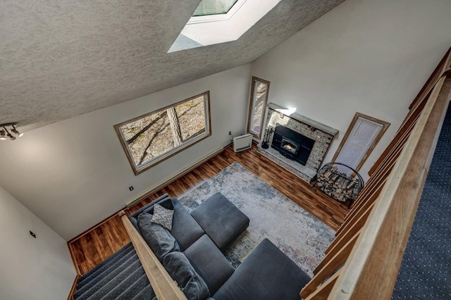 living room featuring a glass covered fireplace, lofted ceiling with skylight, wood finished floors, and a textured ceiling