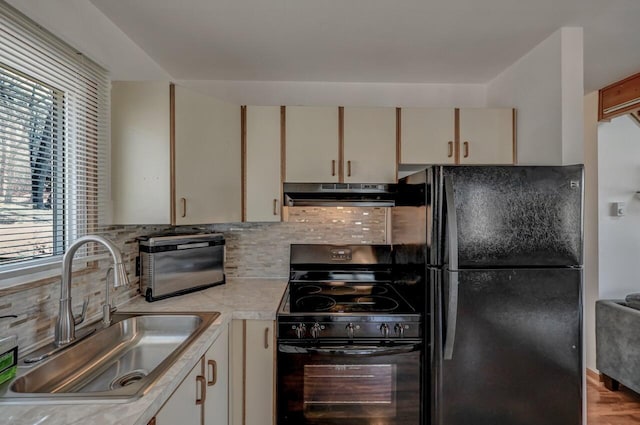 kitchen with under cabinet range hood, light countertops, cream cabinetry, black appliances, and a sink