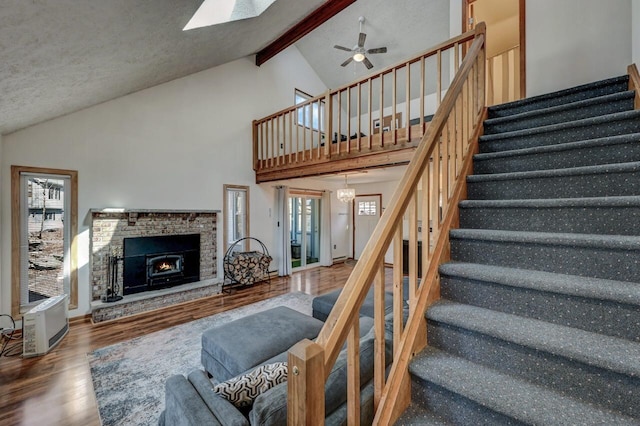 living area with wood finished floors, ceiling fan, stairs, a lit fireplace, and beamed ceiling