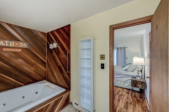 bathroom featuring connected bathroom, wood finished floors, wood walls, and a whirlpool tub