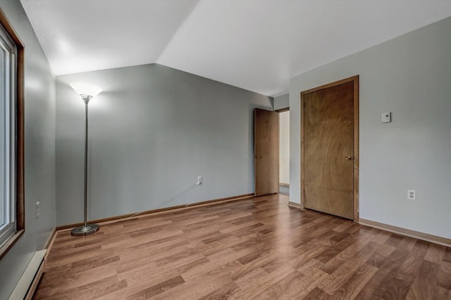 spare room featuring vaulted ceiling, wood finished floors, baseboards, and a baseboard radiator