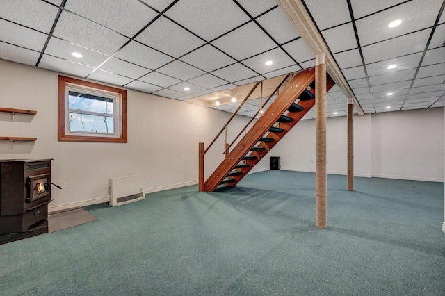 below grade area with heating unit, stairway, carpet flooring, baseboards, and a wood stove