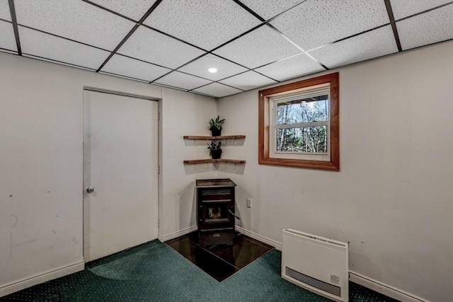 interior space with a drop ceiling, baseboards, and a wood stove