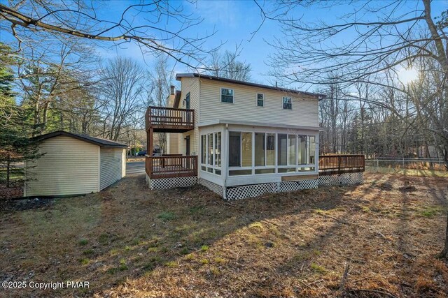 rear view of house featuring a sunroom, an outdoor structure, a wooden deck, and fence