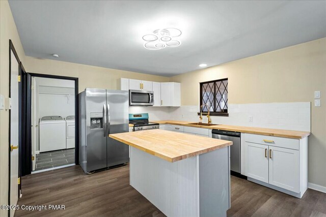 kitchen featuring separate washer and dryer, butcher block counters, a sink, appliances with stainless steel finishes, and dark wood-style floors