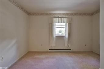 carpeted empty room featuring a baseboard heating unit